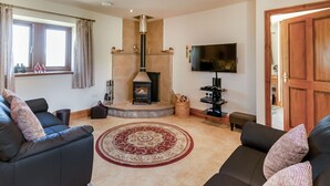 A living room with a fireplace, a television, and two sofas. - Routster Cottage (Settle)