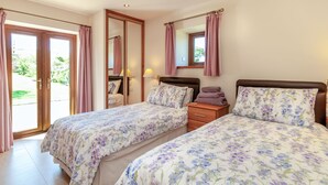 A bedroom with two beds, a wooden nightstand, a mirror, and a window with curtains. - Routster Cottage (Settle)