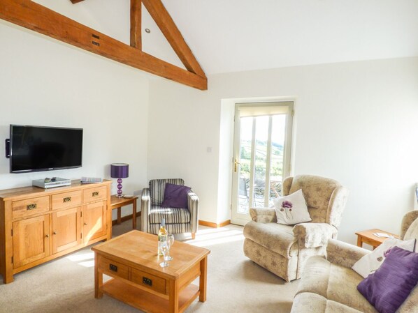 A living room with a television, wooden furniture, a striped chair, and a sofa with a view to the outdoors. - Ghyll Bank Byre (Kendal)