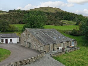 A stone farmhouse with a gravel driveway and a small white building adjacent to it. - Ghyll Bank Byre (Kendal)