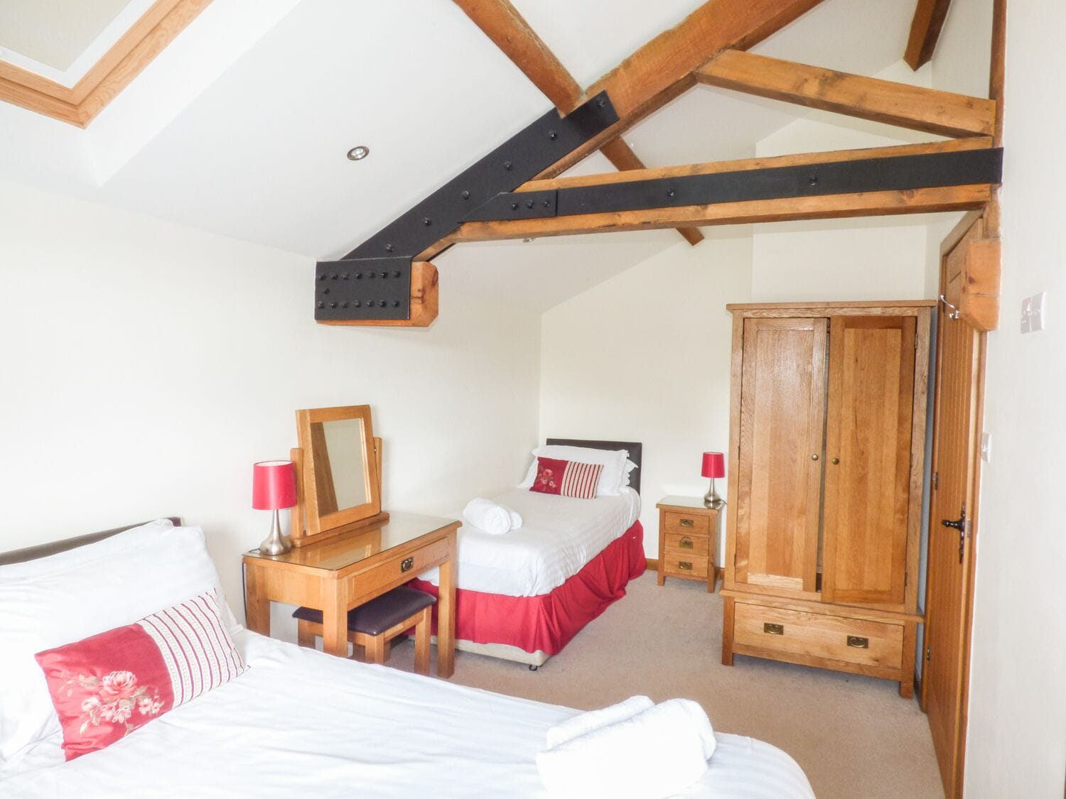 A bedroom with two beds, a wooden desk, a wardrobe, and a mirror.