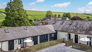 A traditional building with a gravel courtyard, wooden fences, and multiple windows. - Corner Barn (Blandford Forum)