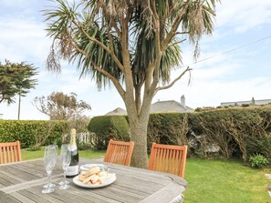 An outdoor dining table with chairs, a bottle of champagne, and a plate of food. - Bolenowe (Wadebridge)