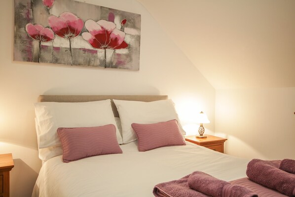 Ein Schlafzimmer mit einem Bett, Kissen, einem Nachttisch, einer Lampe und einem Bild an der Wand.