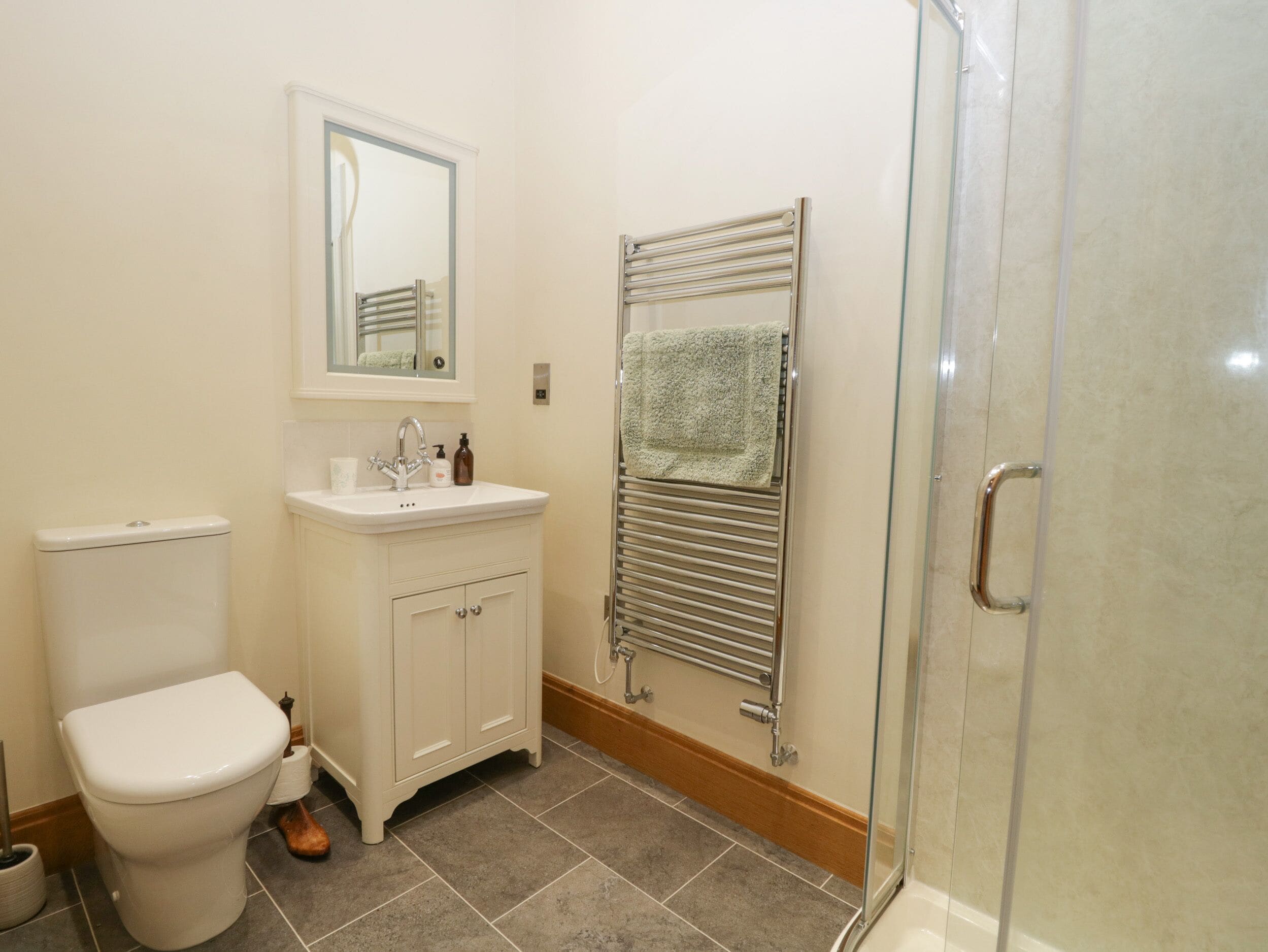 A bathroom with a toilet, sink, mirror, towel rack, and glass shower enclosure.