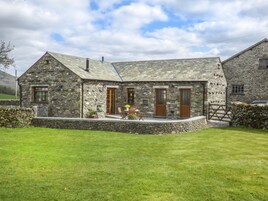 Une maison en pierre avec un porche à l’avant, un petit jardin et un mur en pierre.