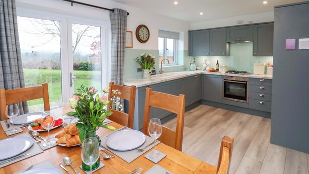 A modern kitchen with grey cabinets, a built-in oven, and a dining area with a wooden table set for a meal.