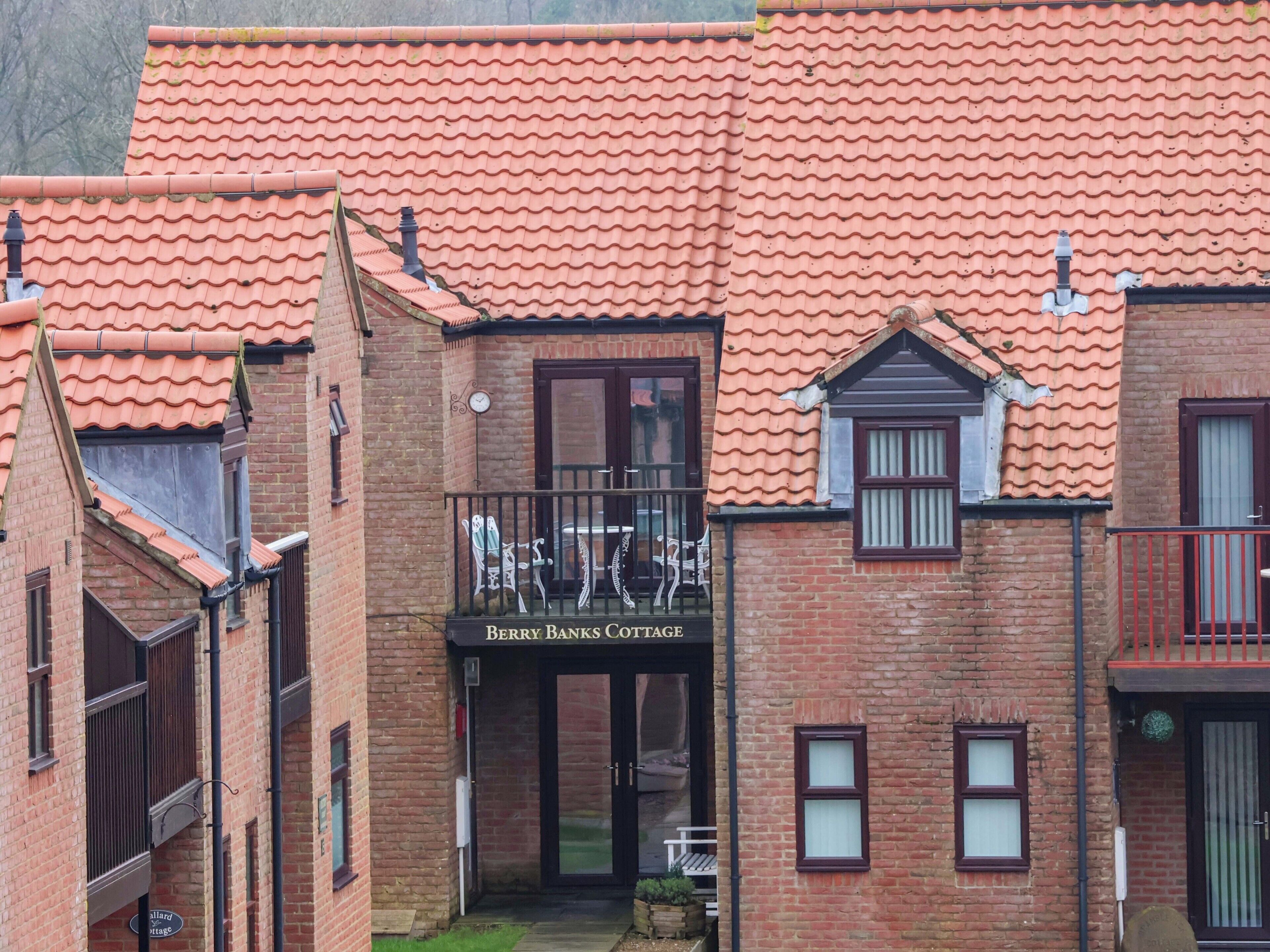 A brick building with a red-tiled roof and a sign reading "Berry Banks Cottage."