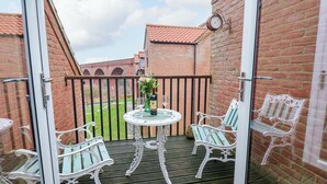 A balcony with a round table, two chairs, a clock, and a brick wall.
