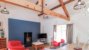 A living room with a fireplace, red chairs, a TV, and a dining table. - Hen Blas (Pwllheli)