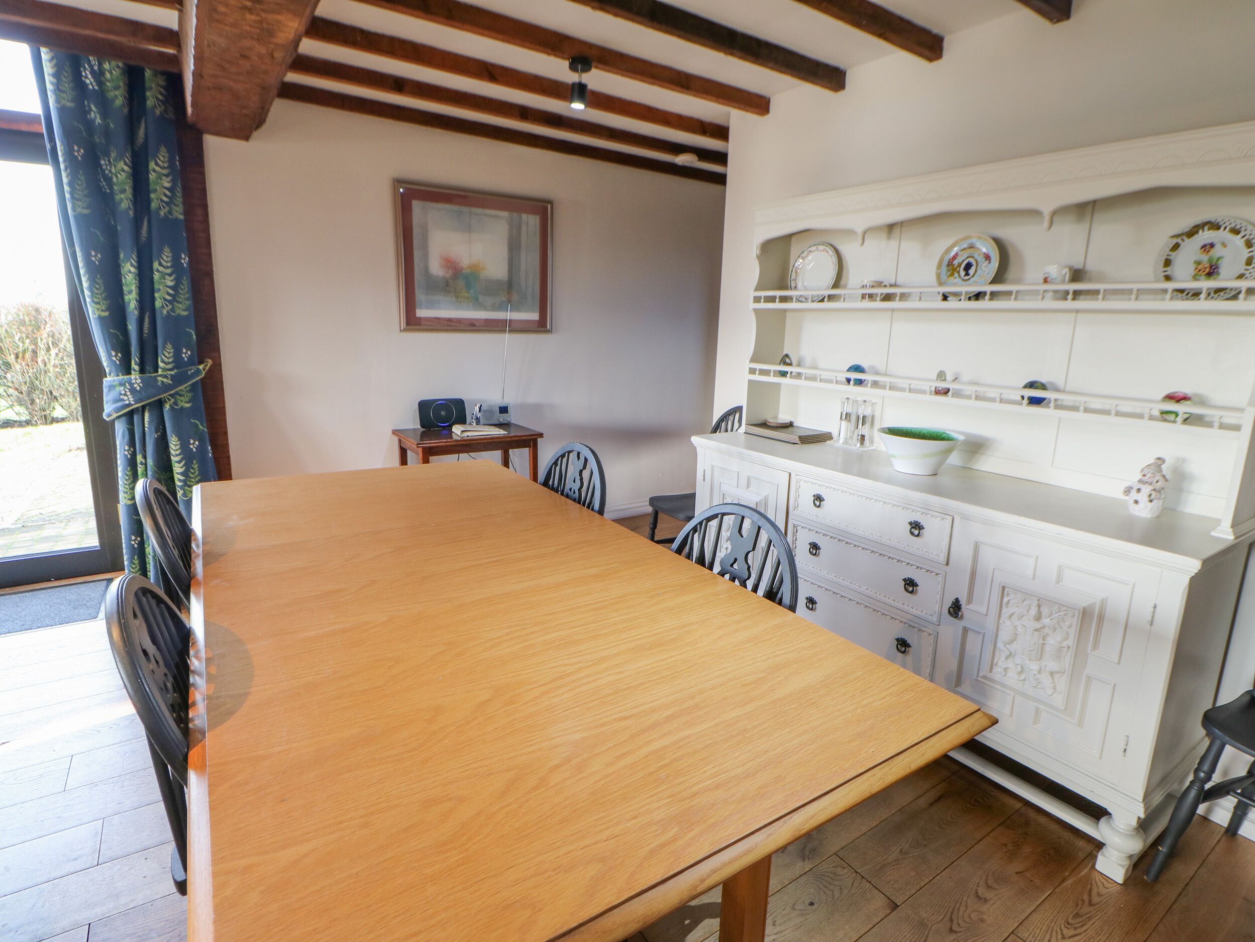 Un comedor con una mesa de madera, sillas, un armario blanco con platos decorativos y un cuadro en la pared.