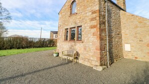 A stone building with a sloped roof, a window, and a bench outside. - Hadrian's View (Brampton)