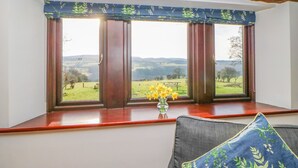 A room with a large window overlooking a rural landscape, a wooden beam ceiling, and a vase with flowers on the windowsill. - Hadrian's View (Brampton)