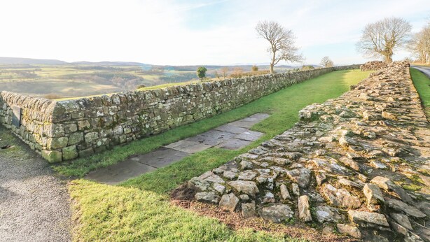 A stone wall with a grassy path leading to a stone structure. - Hadrian's View (Brampton)