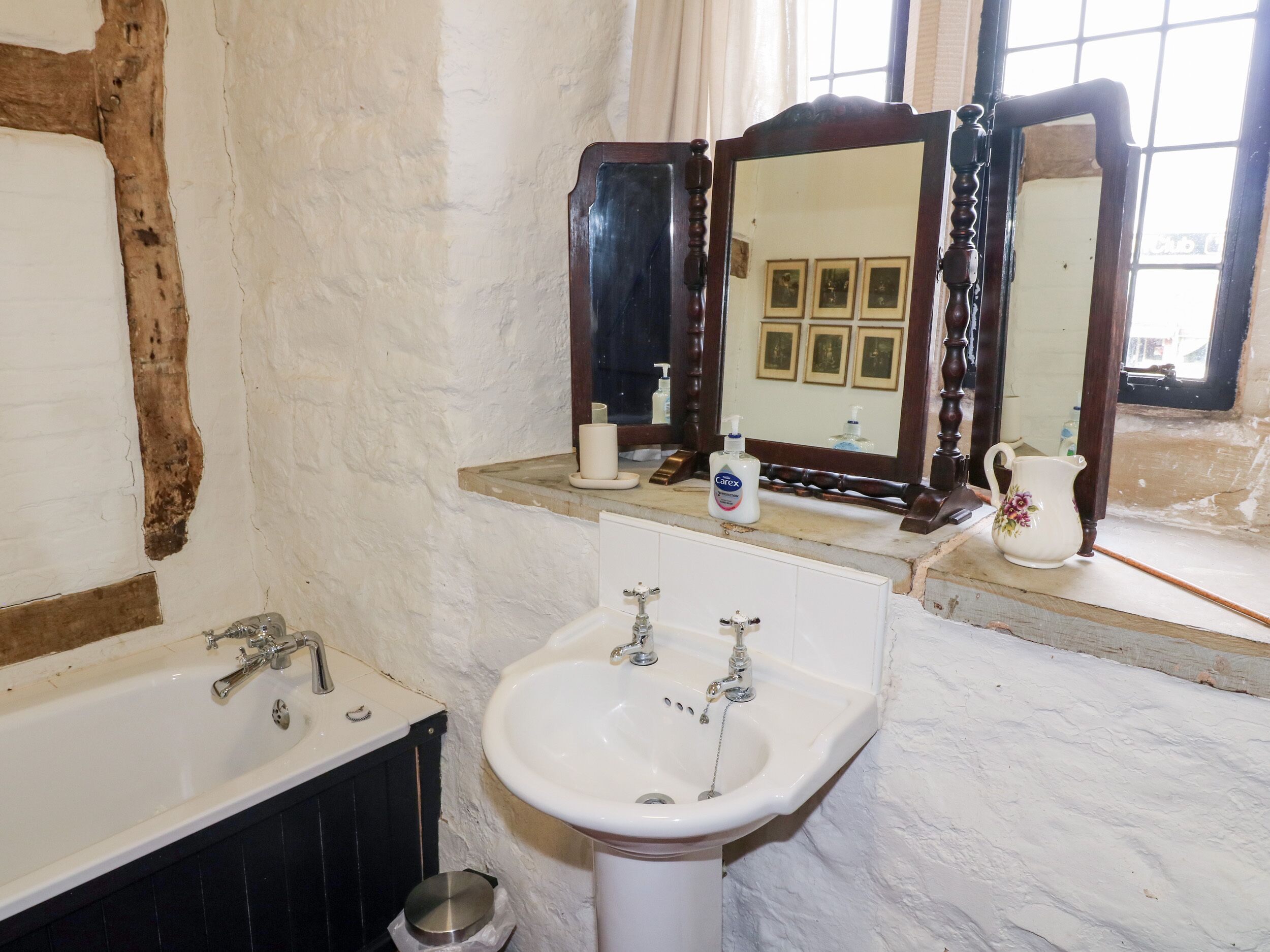 Un baño con un lavamanos blanco, una bañera y un espejo sobre el lavamanos.