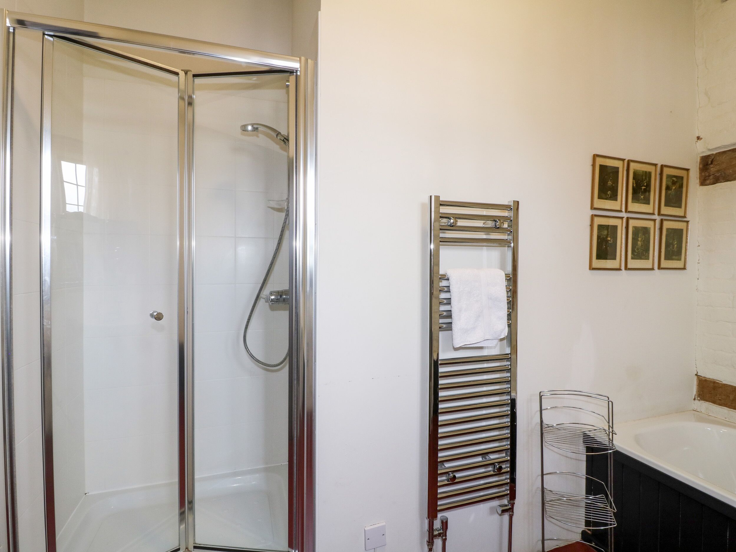 A bathroom with a glass-enclosed shower, a towel rack with a white towel, and a bathtub.