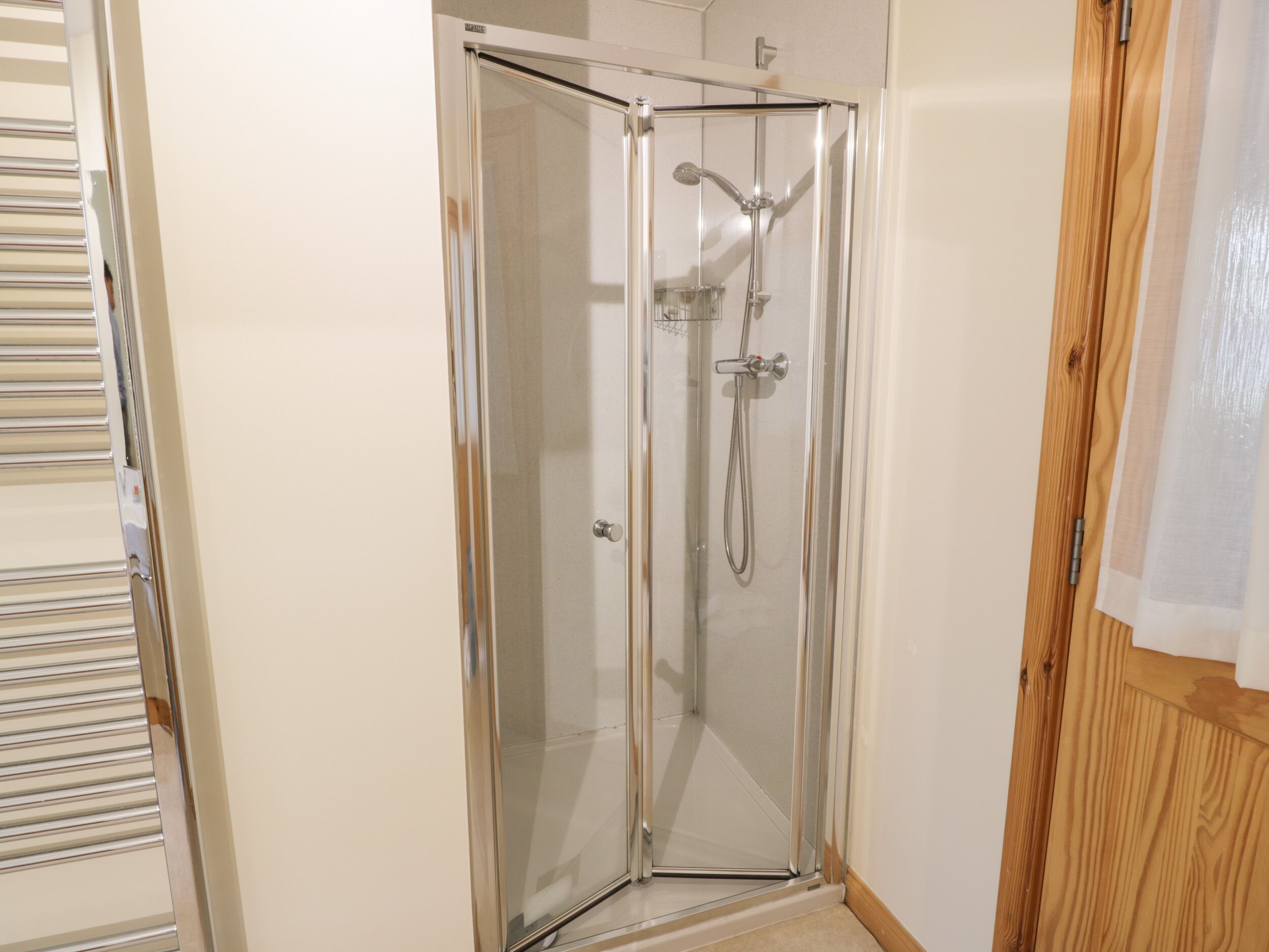 A glass-enclosed shower with a handheld showerhead and a wall-mounted faucet.