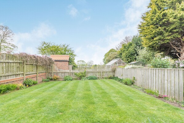 A well-maintained backyard with a wooden fence, a brick house, and various plants. - Fisher Cottage (Hornsea)