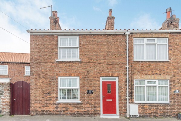 A two-story brick house with a red door, numbered 33, and a small attached garage.
