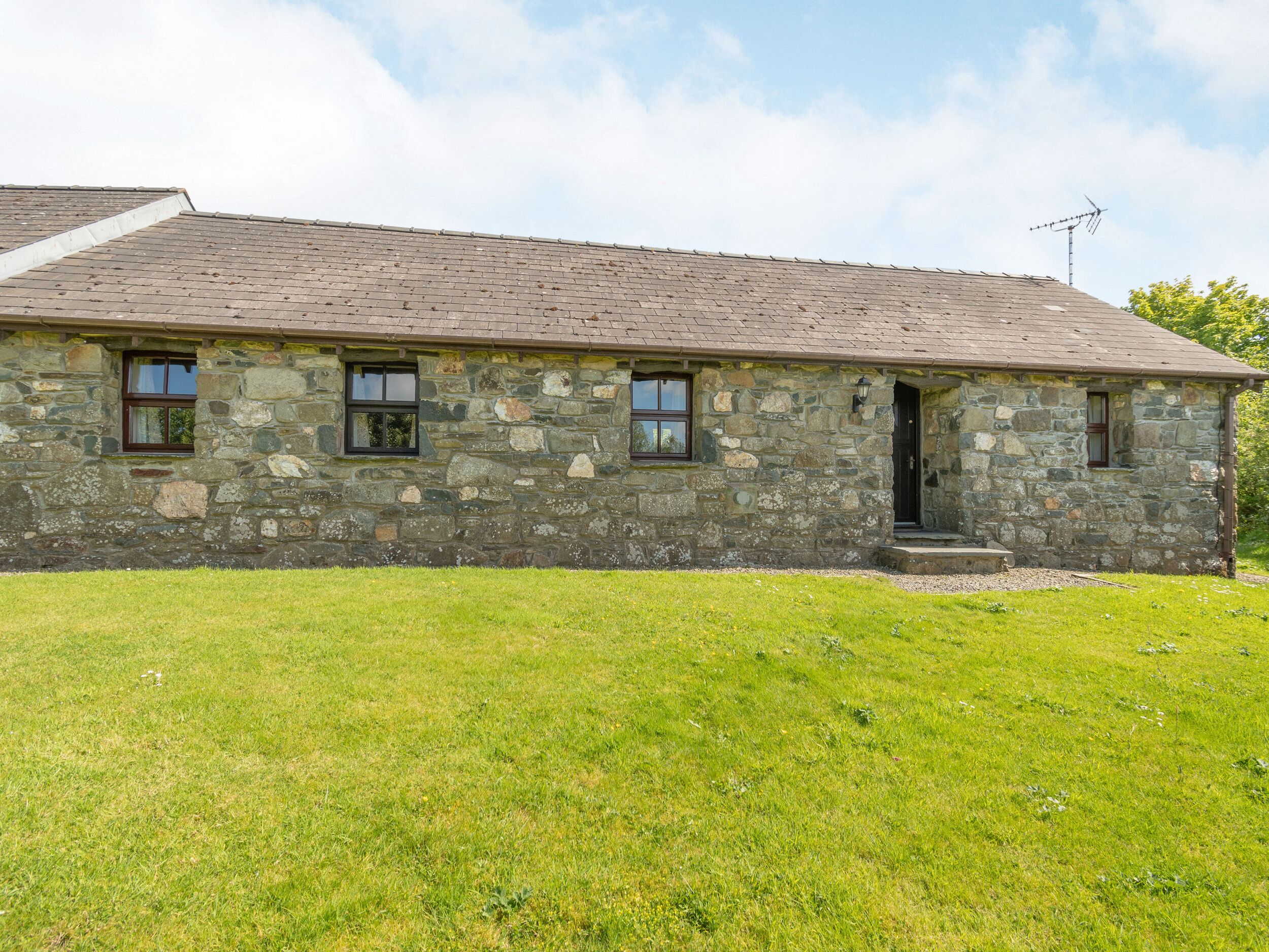 A stone building with a sloped roof, a small porch, and a grassy yard.