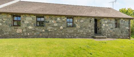 A stone building with a sloped roof, a small porch, and a grassy yard.