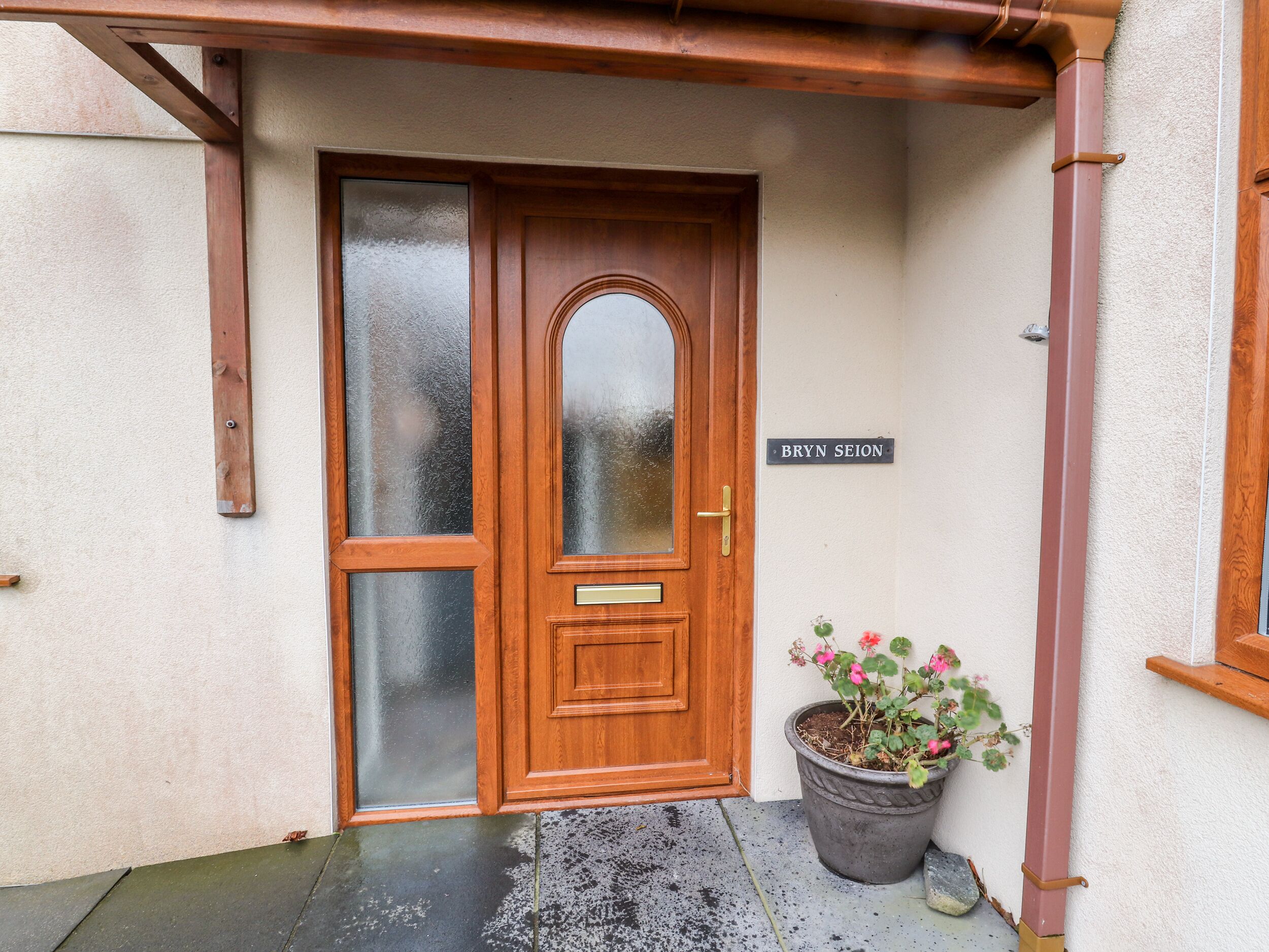 Una puerta de madera con un panel de vidrio esmerilado, un pomo de latón y una placa con el nombre 'BRYN SEION'.