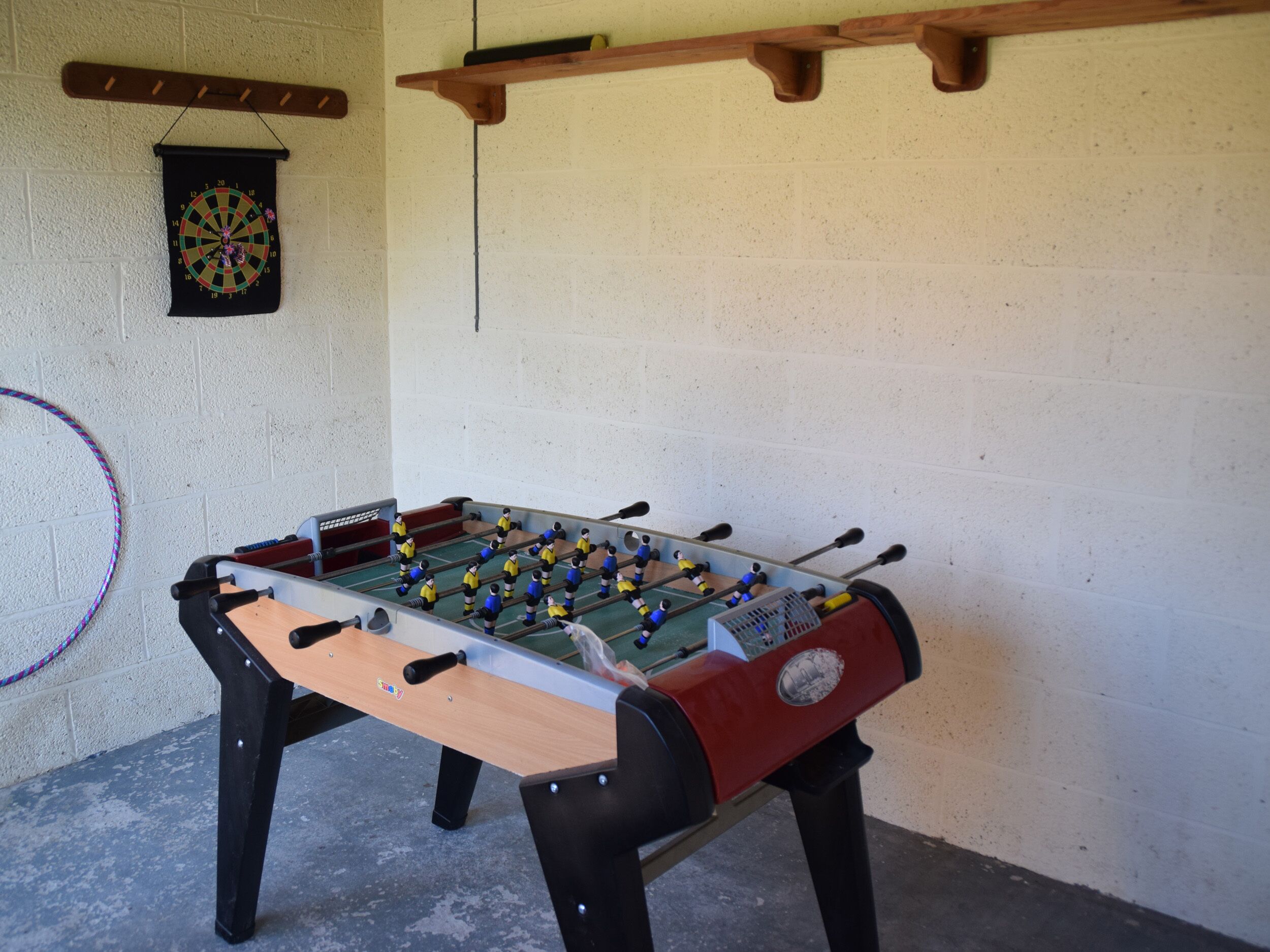 A foosball table in a room with a dartboard and a hula hoop on the wall.