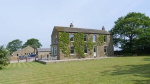 A stone building with a sloped roof and ivy-covered walls, a lawn in front, and a clear sky. - Cringles House (Keighley)