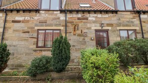 Un bâtiment en pierre avec un toit recouvert de tuiles, deux fenêtres avec volets et une porte.