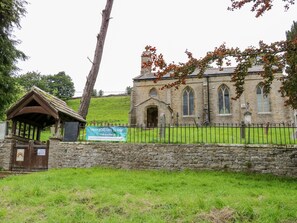 A stone church with a signboard, a wooden shelter, and a grassy area in front. - Margaret's Cottage (Richmond)
