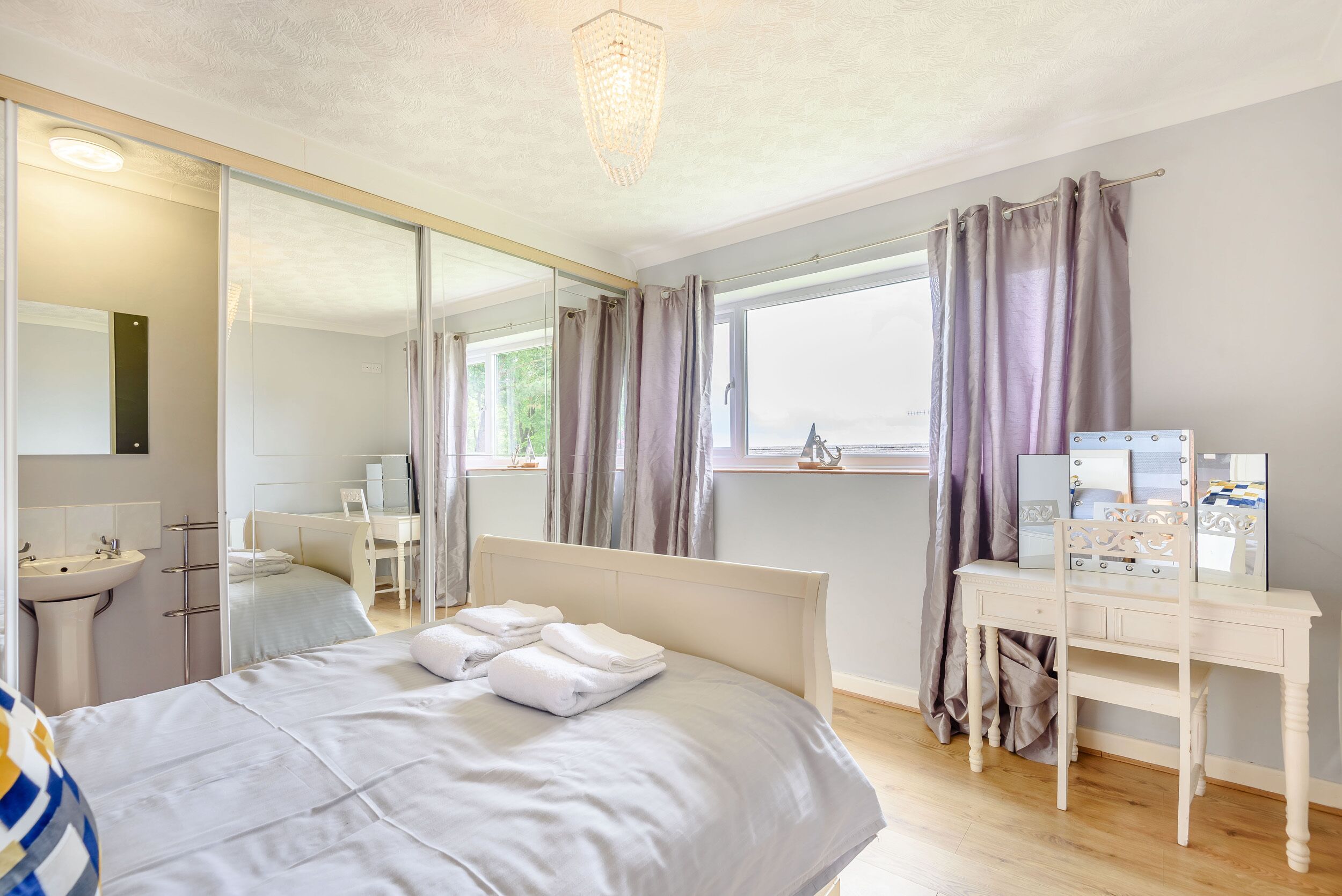 A bedroom with a bed, a vanity with a mirror, a desk, and a window with curtains.