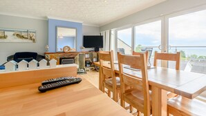Uma sala de jantar com móveis de madeira, uma televisão e vista para o mar.