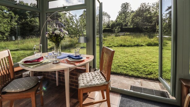 A conservatory with a table set for two, chairs, and a vase of flowers. - Wood Glen Cottage (Heathfield)