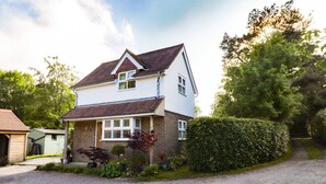 A two-story house with a sloped roof, a front porch, and a gravel driveway. - Wood Glen Cottage (Heathfield)