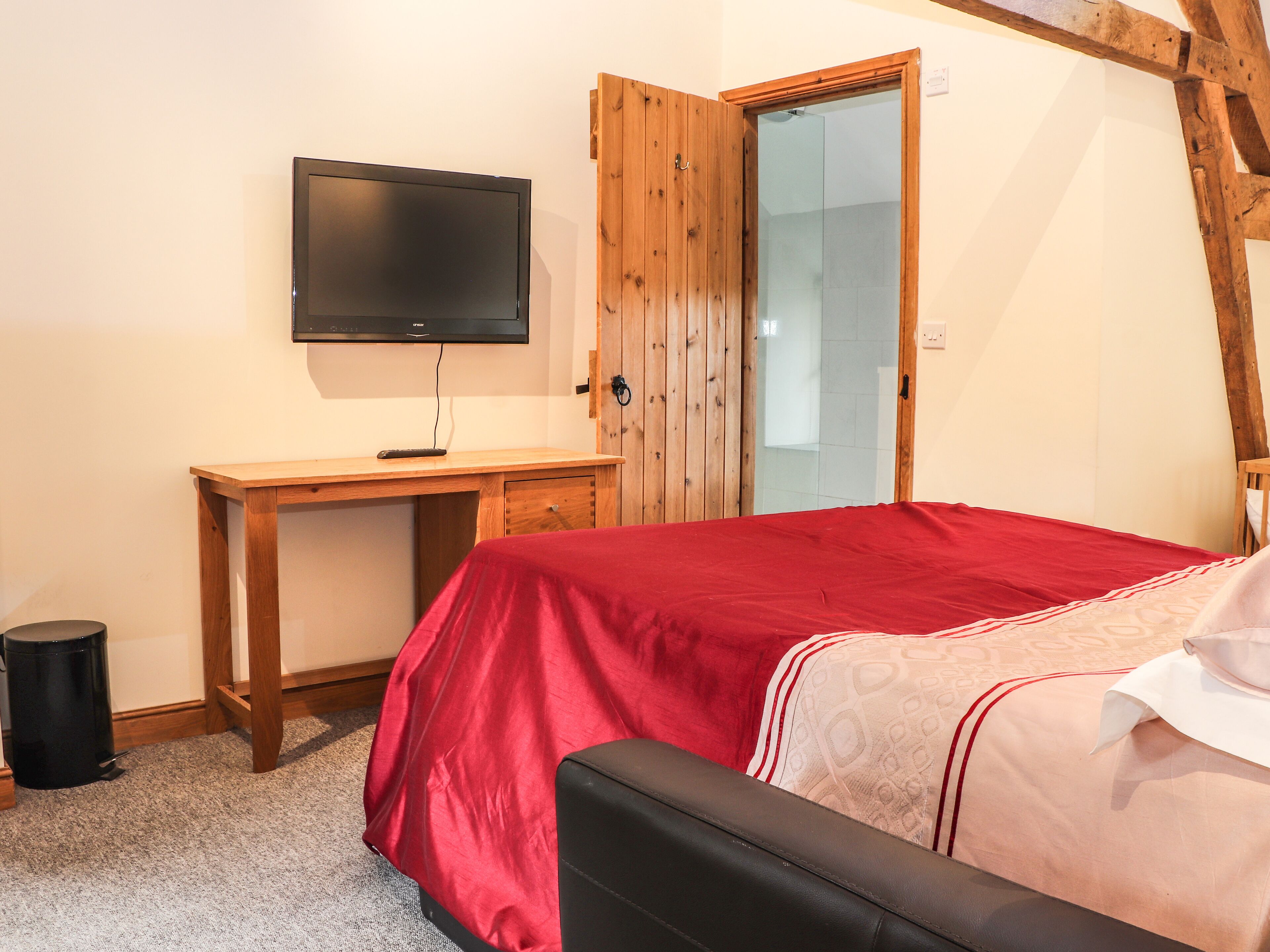 Un dormitorio con una cama, un escritorio de madera, un televisor y una puerta que da a un baño.