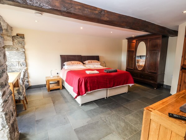 A bedroom with a bed, wooden headboard, stone wall, and a wooden cabinet. - Maestyddyn Farm House (Ruthin)