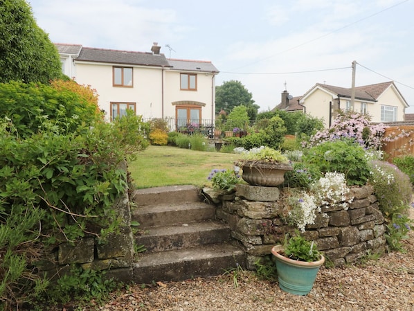 A residential house with a stone staircase leading to the front door, surrounded by a well-maintained garden with various plants and flowers.