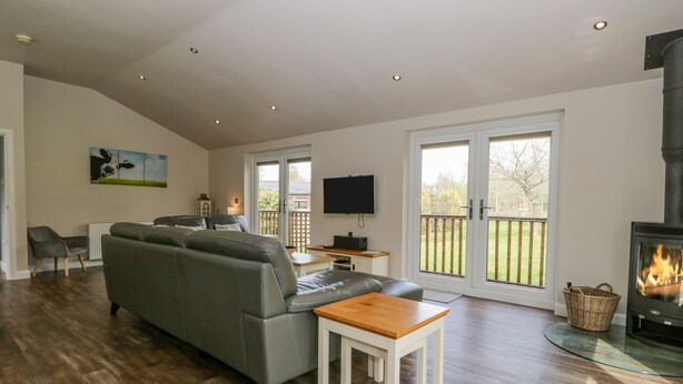 Een ruime woonkamer met een grijze bank, houten vloeren, een aan de muur bevestigde televisie en een open haard.