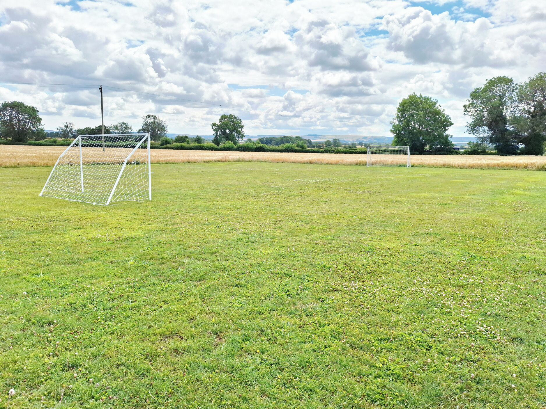 Un terrain de football avec deux buts, entouré d’arbres et bordé de champs ouverts.