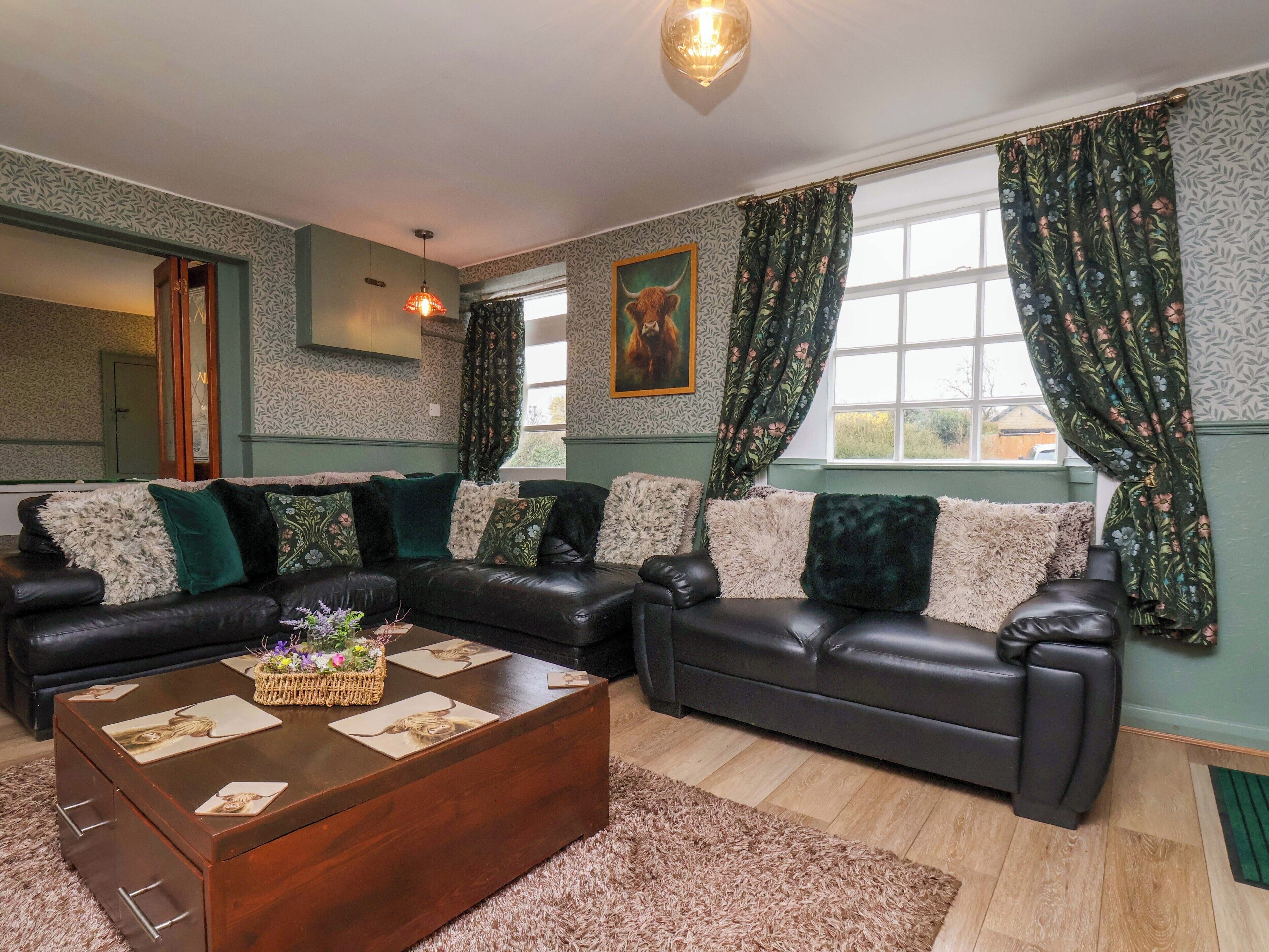 A living room with a dark leather sofa, a wooden coffee table, and patterned curtains.