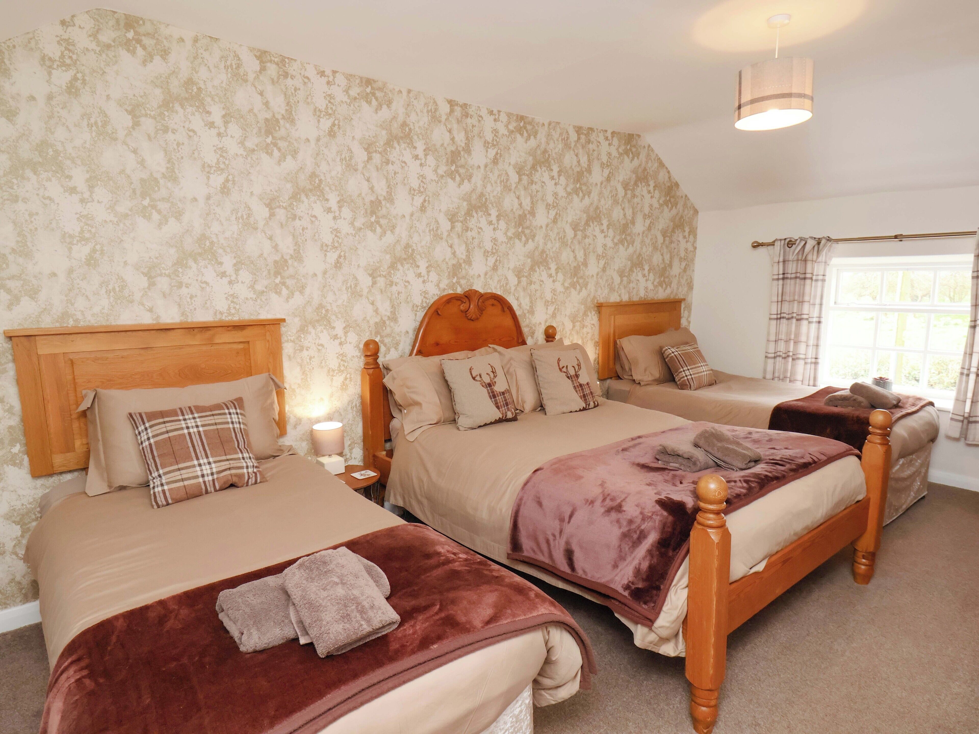 A room with two beds, a wooden headboard, a nightstand with a lamp, and a window with curtains.