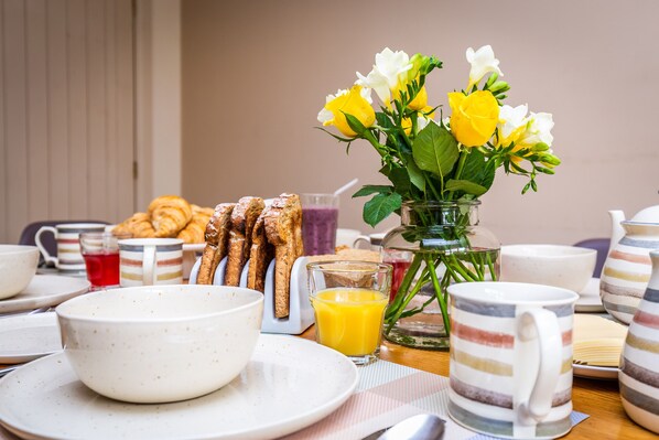 A breakfast setting with plates, bowls, a glass of orange juice, croissants, and a vase with flowers. - Broadleaf Lodge (Lincoln)