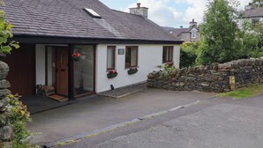 A white building with a dark roof, stone wall, and a small garden area with flowers. - Becks Fold (Coniston)