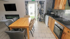 Una cocina moderna con comedor, que incluye una mesa y sillas de madera, horno empotrado y televisor de pantalla plana montado en la pared.