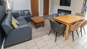 Una sala de estar con un sofá, una mesa de centro, una mesa de comedor con sillas, un televisor de pantalla plana y una chimenea.