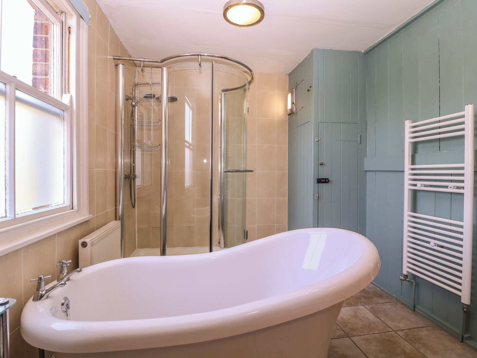 Un baño con una bañera independiente, cabina de ducha con mampara de vidrio y un perchero para toallas.