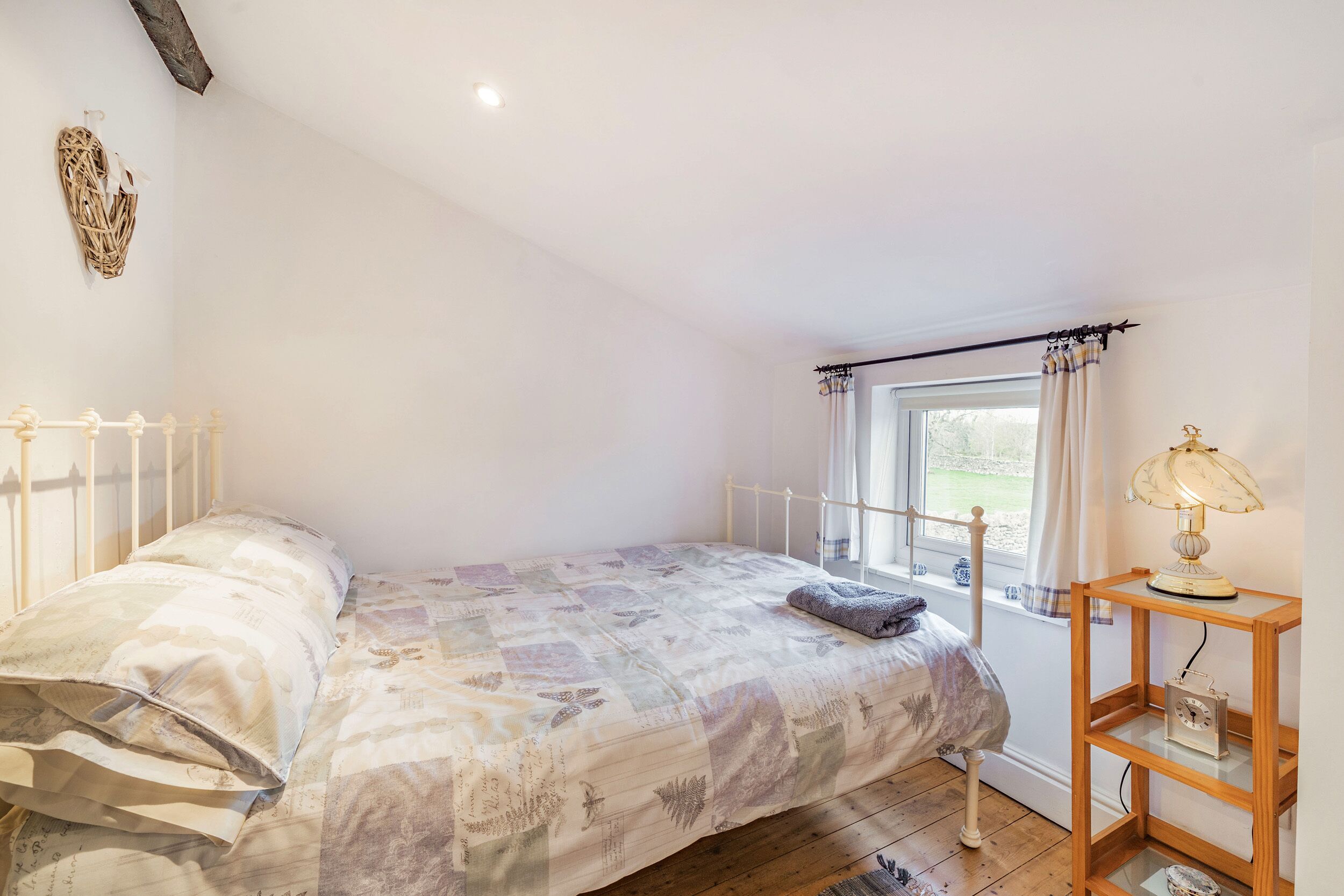Een slaapkamer met een bed, een raam met gordijnen, een nachtkastje met een lamp en een wandplank.