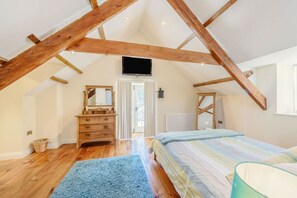 Une chambre avec des poutres en bois, un lit, une commode, un miroir et un téléviseur.