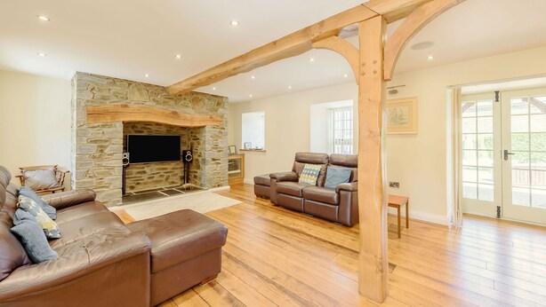 Ein geräumiges Wohnzimmer mit Kamin aus Stein, Ledersofas, Holzböden und einem großen Balkenbau.