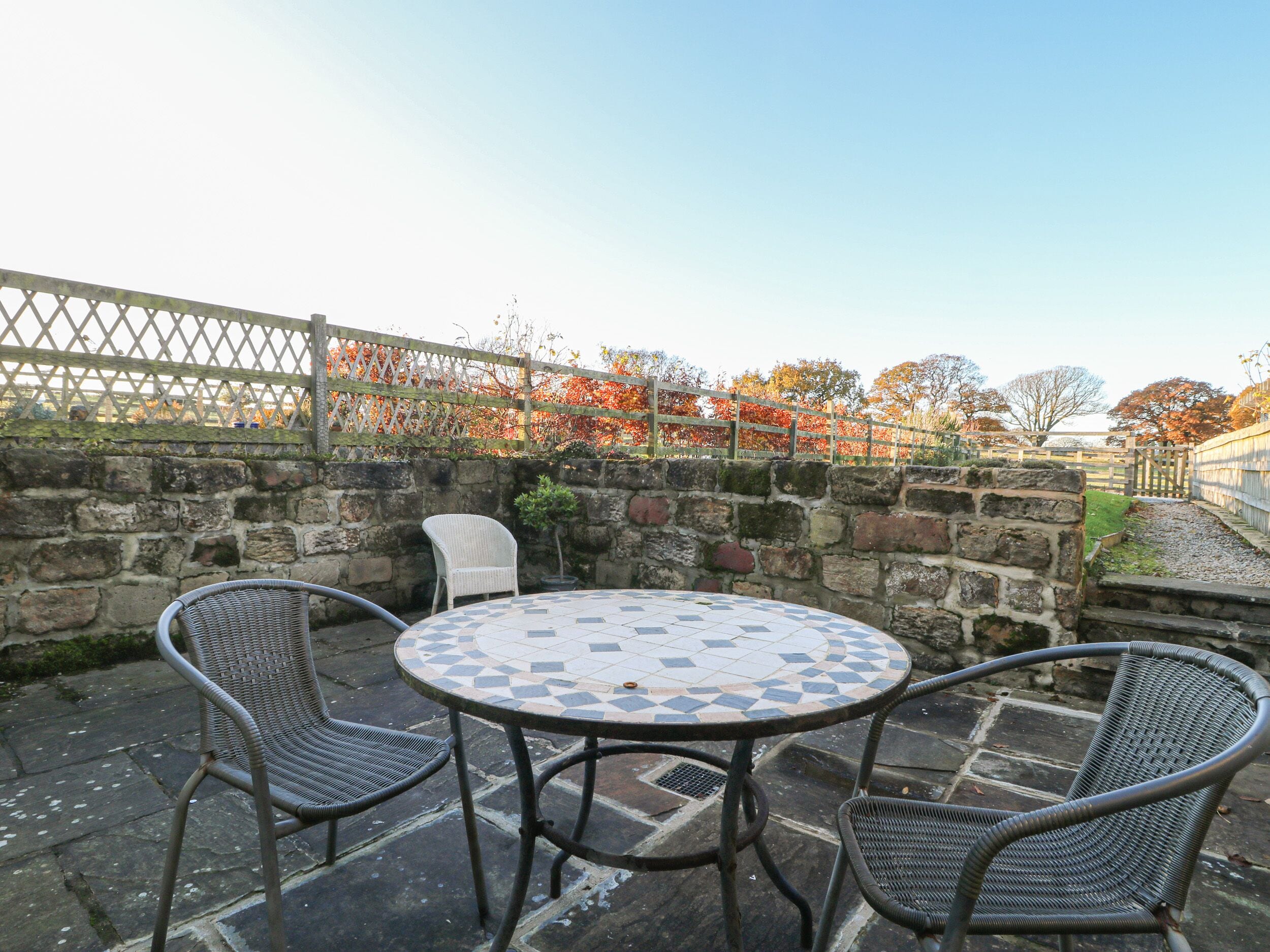 A round outdoor table with a mosaic tile top, surrounded by wicker chairs.